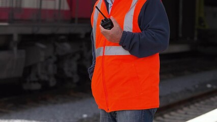 4K slow motion footage of railway attendant in reflective orange vest holding radio. Locomotive moving in slow motion stock video.
