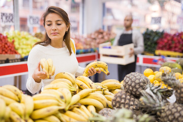 Fototapeta na wymiar Cute woman picks ripe bananas at grocery supermarket