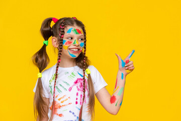 A little girl with bright colors painted, a little girl is fond of drawing, A child with paints on a yellow isolated background. Children's leisure, a schoolgirl at a drawing course.