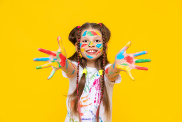 A little girl with bright colors painted, a little girl is fond of drawing, A child with paints on a yellow isolated background. Children's leisure, a schoolgirl at a drawing course.