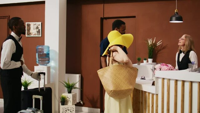 Tourists leaving hotel accommodation, ending honeymoon trip after giving access key card to receptionist and doing checkout process. Hotel guests at departure in lobby. Handheld shot.