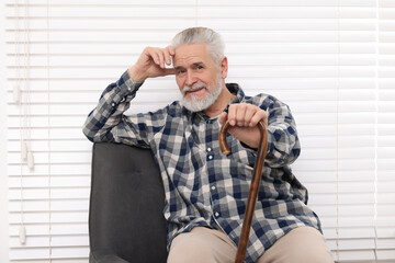 Senior man with walking cane sitting on armchair at home