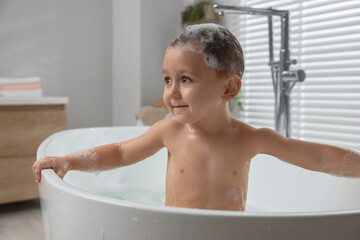 Cute little boy washing hair with shampoo in bathroom