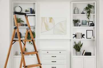 Wooden folding ladder near chest of drawers and shelves with accessories indoors