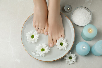 Woman soaking her feet in bowl with water and flowers on grey marble floor, above view. Pedicure...