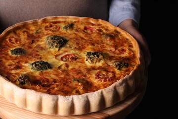 Woman holding delicious homemade vegetable quiche on black background, closeup