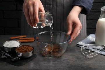 Making dalgona coffee. Woman pouring water into bowl at grey table, closeup