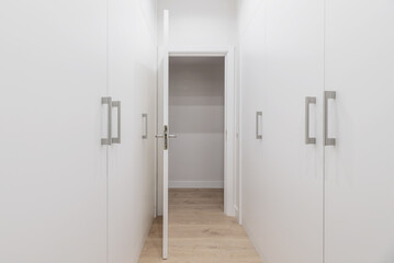A walk-in closet with white wooden door cabinets on both