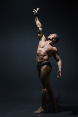 A muscular athlete stretches his arm up, striving for the ideal, a concept. Contrast photo on dark
