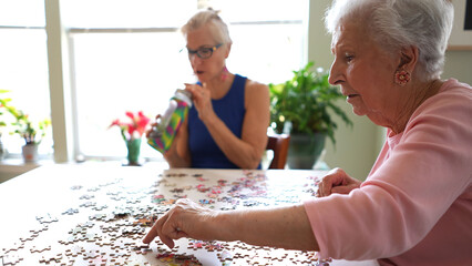 Two happy elderly mature women talking and playing with puzzle pieces.