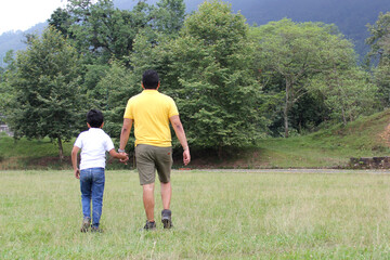 Fototapeta na wymiar Divorced single dad and 9-year-old son, brown-haired Latino, walk through countryside looking to the future together hand in hand