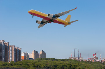 Fototapeta premium A jet cargo airliner comes in for a landing over a forest, public housing and industrial area. Close-up of the engine and wing mechanization. The concept of cargo delivery by air. Sunny morning.