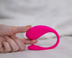Woman holding curved pink vibrator while lying in bed.  - obrazy, fototapety, plakaty