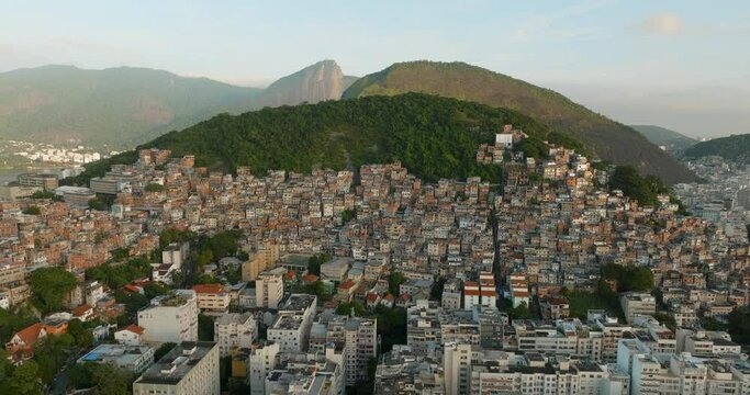 Flying slowly above shanty town buildings on the mountainside with Christ the Redeemer in background, Rio de Janeiro, Brazil. Wide angle view