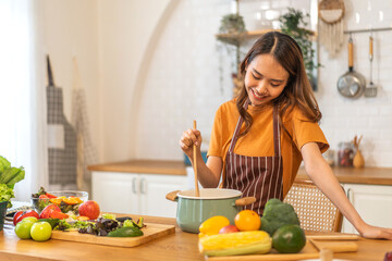 Young woman standing near stove and cooking.Happy woman looking and smelling tasting fresh delicious from soup in a pot with steam at white interior kitchen