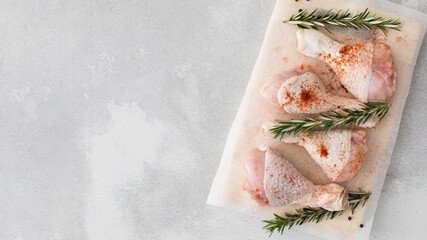 Raw chicken legs with spices and rosemary sprigs on a wooden cutting board. Copy space - obrazy, fototapety, plakaty