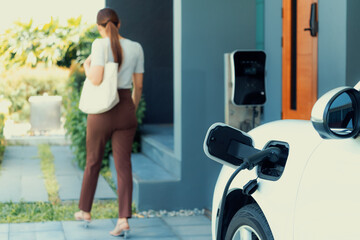 Focus EV charger plugged into EV car at home charging station with blurred background of...