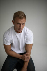 handsome male actor model posing sitting on armchair in studio in white t-shirt.