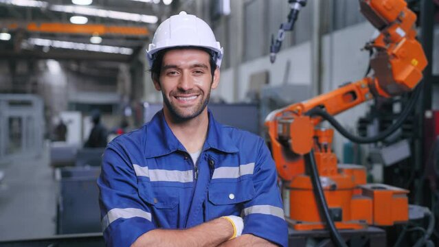 Engineer man in safety uniform crossed arms smiling looking at camera have confidence front of welding robot at steel industry. Factory and warehouse concept