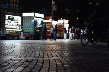 Obraz premium Brick Sidewalk at Night in New York City, Blurred Vendors on Street