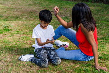 Happy mother and son using mobile phone together in a park.