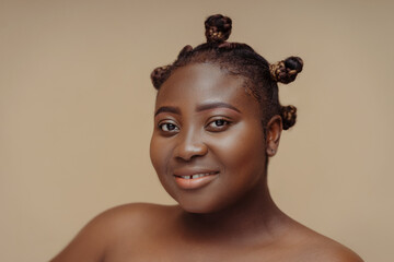 Closeup portrait of beautiful smiling African American woman with stylish hair  looking in mirror isolated on beige background. Skin care, makeup,  natural beauty, body positive concept