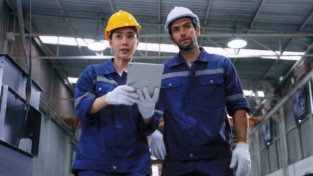 Smart engineer worker man and woman in uniform safety and wear helmet consulting and using tablet help analyze data in warehouse at manufactory. Industrial and factory warehouse concept
