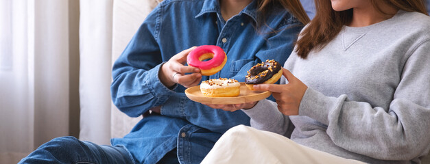 Closeup image of a young couple women holding and eating donuts together