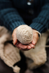 Abuela en la sala de casa feliz y concentrada, usando unos palitos de tejer y lana de oveja,...
