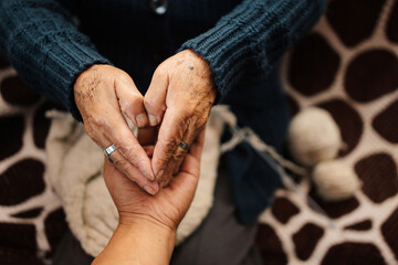 Abuela en la sala de casa feliz y concentrada, usando unos palitos de tejer y lana de oveja,...