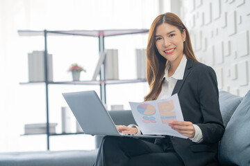 Image of a young beautiful Asian Business woman smiling while working with a laptop and talking to work doing math finance on an office desk, tax, report, accounting, statistics, and research concepts