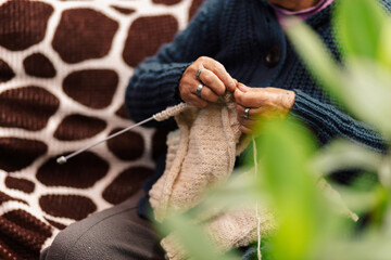 Mujer latina, adulto mayor , feliz y concentrada, en la sala de casa usando unos palitos de tejer y lana de oveja, concepto de vida cotidiana tradicional, tejedora tradicional, enfoque selectivo.