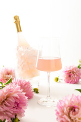 A glass with rose sparkling wine surrounded by dahlias, a bottle of rose sparkling wine is chilled in a glass bucket with ice