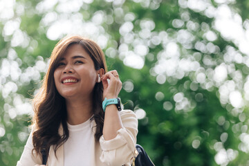 Portrait of a smiling young asian woman listening to music with earphones outdoors