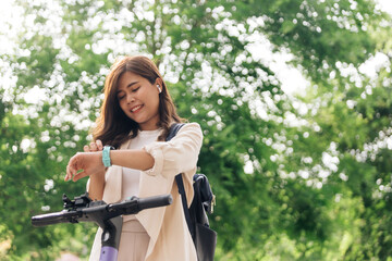 Fototapeta na wymiar happy young asian woman in earphones looking at wristwatch while riding bicycle in park
