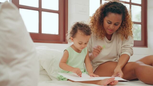 Mother and baby girl child drawing picture in paper by crayon playing laughing on bed in bedroom at home in the morning. Family concept