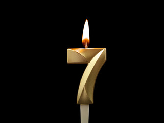 Burning gold birthday candle isolated on black background. Number 7.
