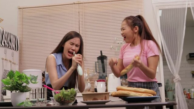 Happy lesbian couple cooking together in kitchen at home dancing and singing at dining table. The concept of modern living. LGBT couple