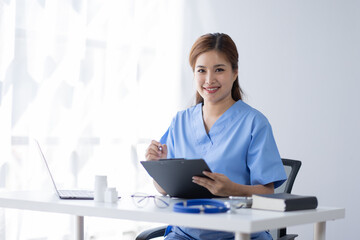 Happy doctor Portrait of young asian woman nurse or doctor smiling using a laptop writing content at consultation