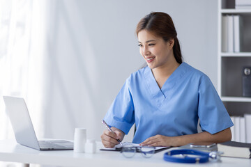 Happy doctor Portrait of young asian woman nurse or doctor smiling using a laptop writing content at consultation