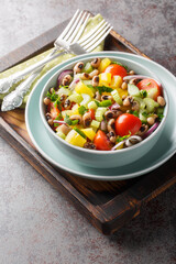 Fresh salad with cherry tomatoes, celery, yellow pepper, black-eyed peas, cucumber and onion close-up in a bowl on the table. Vertical