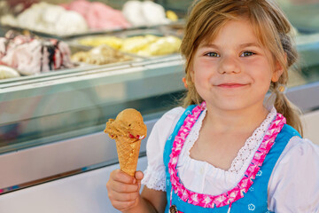 Little preschool girl eating sweet ice cream in waffle cone on sunny summer day. Happy toddler...