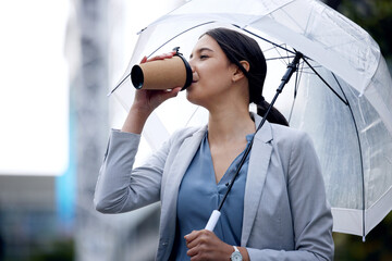 Business woman is drinking coffee, umbrella and travel with commute to work and person in the city. Young female professional in the rain, enjoying hot drink with traveling, urban and insurance