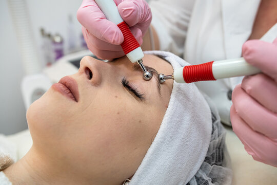 Young pretty woman receiving facial  performing microcurrent stimulation treatment at spa clinic
