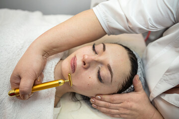 Fototapeta na wymiar woman receive procedure procedure on face with golden pulse facial massager