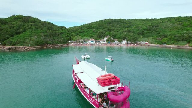 Dolly in establishing aerial view of a tourist boat with people enjoying themselves on the shores of Azeda Beach in B&uacute;zios, Brazil.