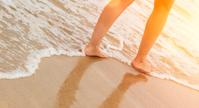 Woman walking on golden sand beach leaving footprints in the sand. Summer beach travel concept.