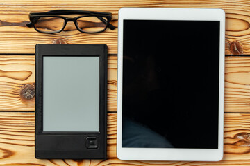 Digital tablet and electronic reader book with glasses on wooden background top view
