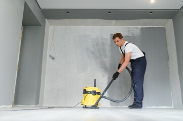 A worker vacuums a room after repairing the floors. Apartment after renovation with a vacuum...