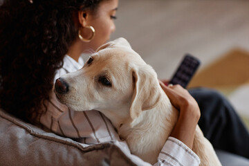 Closeup portrait of cute white puppy cuddling with young woman at home over shoulder